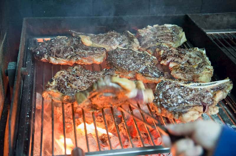 Mano del asador volteando un txuleta en la parrilla